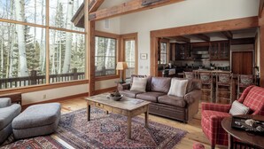 A spacious living room with large windows, a fireplace, and a kitchen area visible through an open door.