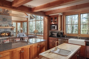 Una cocina amplia con armarios de madera, una chimenea de piedra y ventanas grandes que dan a vistas de árboles.