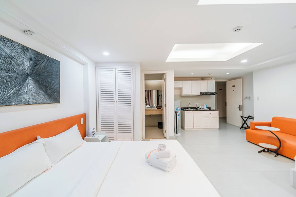 Une chambre d’hôtel moderne équipée d’un lit, d’une salle de bain, d’une cuisine et d’un canapé orange.
