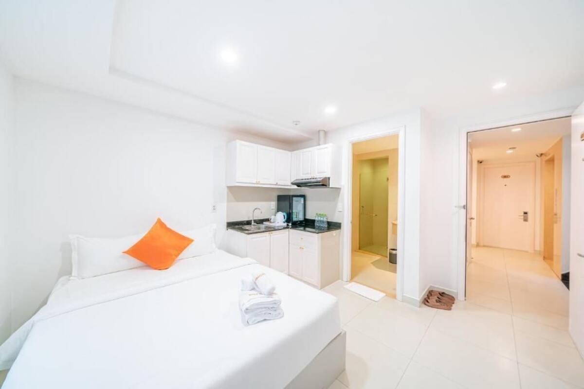 Une chambre d’hôtel avec un lit, une petite kitchenette et une salle de bain visible à travers une porte ouverte.