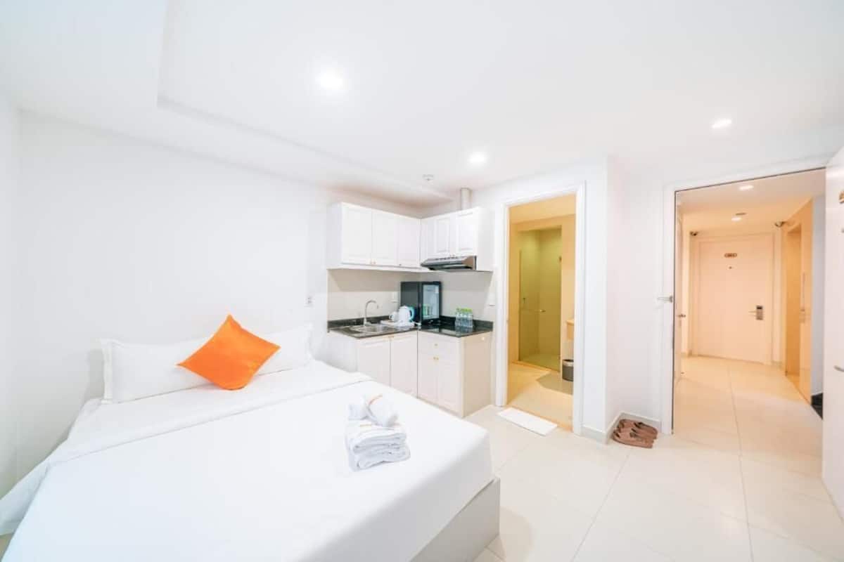 A hotel room with a bed, a small kitchenette, and a bathroom visible through an open door.