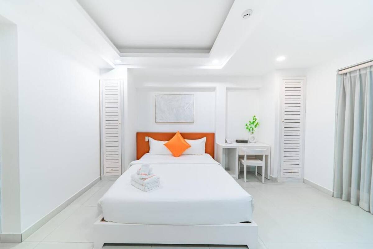 Une chambre d’hôtel moderne, dotée d’un grand lit, d’une table de chevet, d’un petit bureau et d’une fenêtre avec des rideaux.