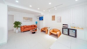 A modern living room with a sofa, armchairs, a coffee table, a potted plant, and a small kitchen area with appliances. - Royal Crown Hotel (Ho Chi Minh City)