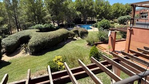 Una piscina rodeada de setos y árboles bien cuidados, con una terraza de madera al frente.
