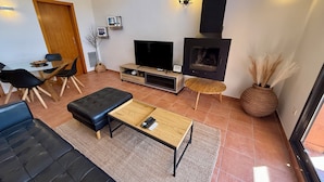 Una sala de estar moderna con sofá, una mesa de centro, televisor, chimenea y un comedor con sillas y una mesa.
