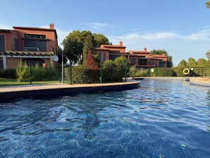 A swimming pool with clear water, surrounded by a fence and trees.
