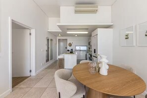 Cozinha moderna com armários brancos, uma ilha central e um espaço de refeições com mesa redonda e cadeiras.