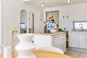 A modern kitchen with white cabinets, a large mirror, and a dining area with a white table and chairs. - Signature Home @ Waterfront Canals (Cape Town)