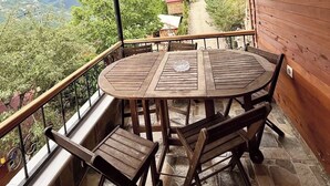 Un balcón de madera con una mesa redonda y sillas, un ventilador de techo y vistas a un paisaje montañoso.