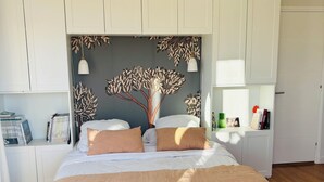Ein Schlafzimmer mit einem großen Bett, einer Holzbank, einer gewobenen Deckenleuchte und einer Wand mit einem Blattmuster.