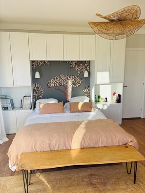 A bedroom with a large bed, a wooden bench, a woven ceiling light, and a wall with a leaf pattern. - Apartment spirit house Ciboure (Urrugne)