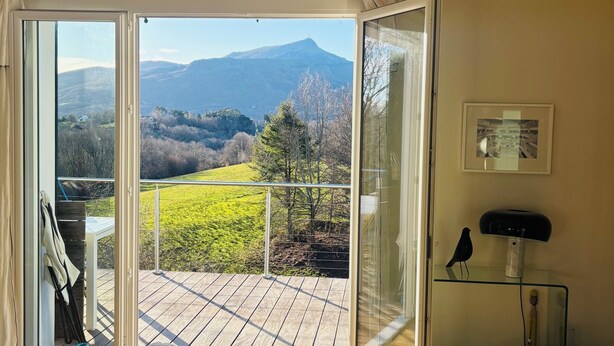 Ein Zimmer mit einer Schiebetür, die auf einen Balkon mit Blick auf Berge und Grün führt.
