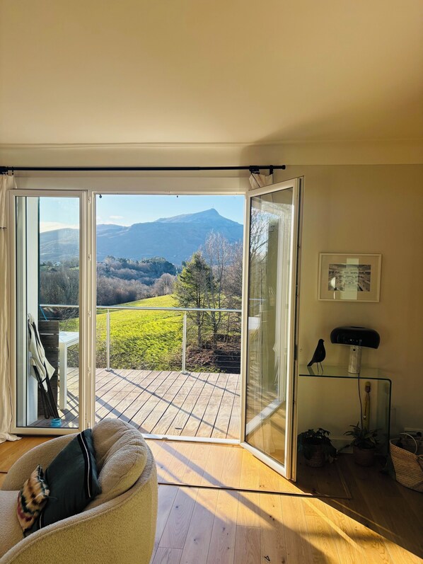 A room with a sliding glass door leading to a balcony with a view of a mountain and greenery. - Apartment spirit house Ciboure (Urrugne)