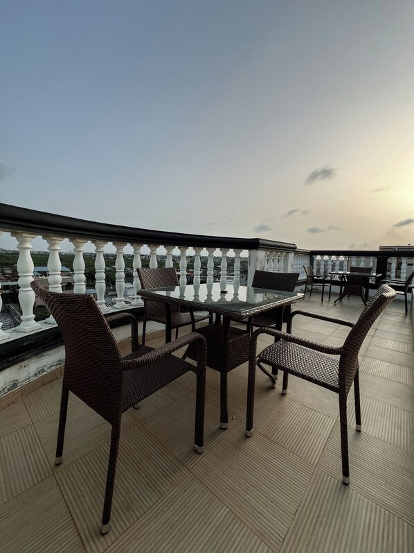 A rooftop terrace with a glass table and wicker chairs, a balustrade, and a cityscape view.