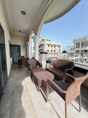 A balcony with wicker furniture, a view of a building under construction, and a clear sky.