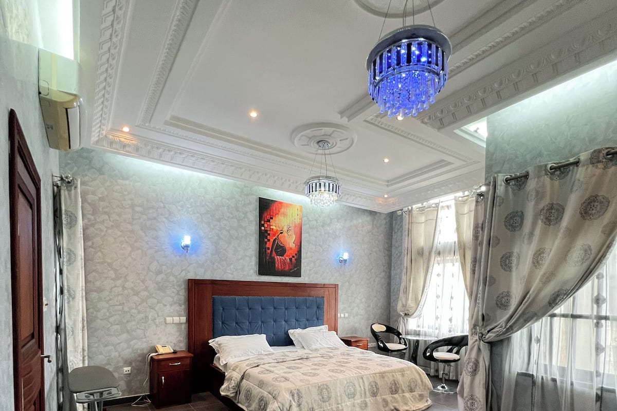 A bedroom with a bed, a desk, a chair, a standing lamp, and a ceiling light fixture.