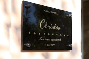 Eine Plakette mit dem Namen 'Christos' und der Aufschrift 'Luxuriöse Wohnung' auf schwarzem Hintergrund mit goldenen Sternen und dem Text 'Gegründet 2022'.