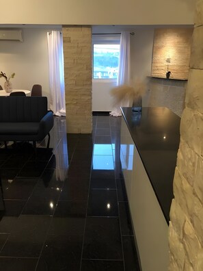 Eine moderne Küche mit schwarzem Arbeitsplatz, einer Wand aus Naturstein und Blick durch ein Fenster.