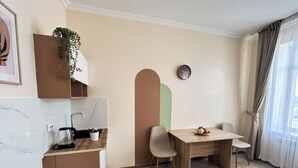 Un espacio habitable compacto con kitchenette, zona de comedor y un amplio ventanal con cortinas.
