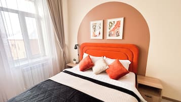 Une chambre à coucher comprenant un lit, une table de chevet, une lampe, une fenêtre avec des rideaux et deux tableaux accrochés au mur.