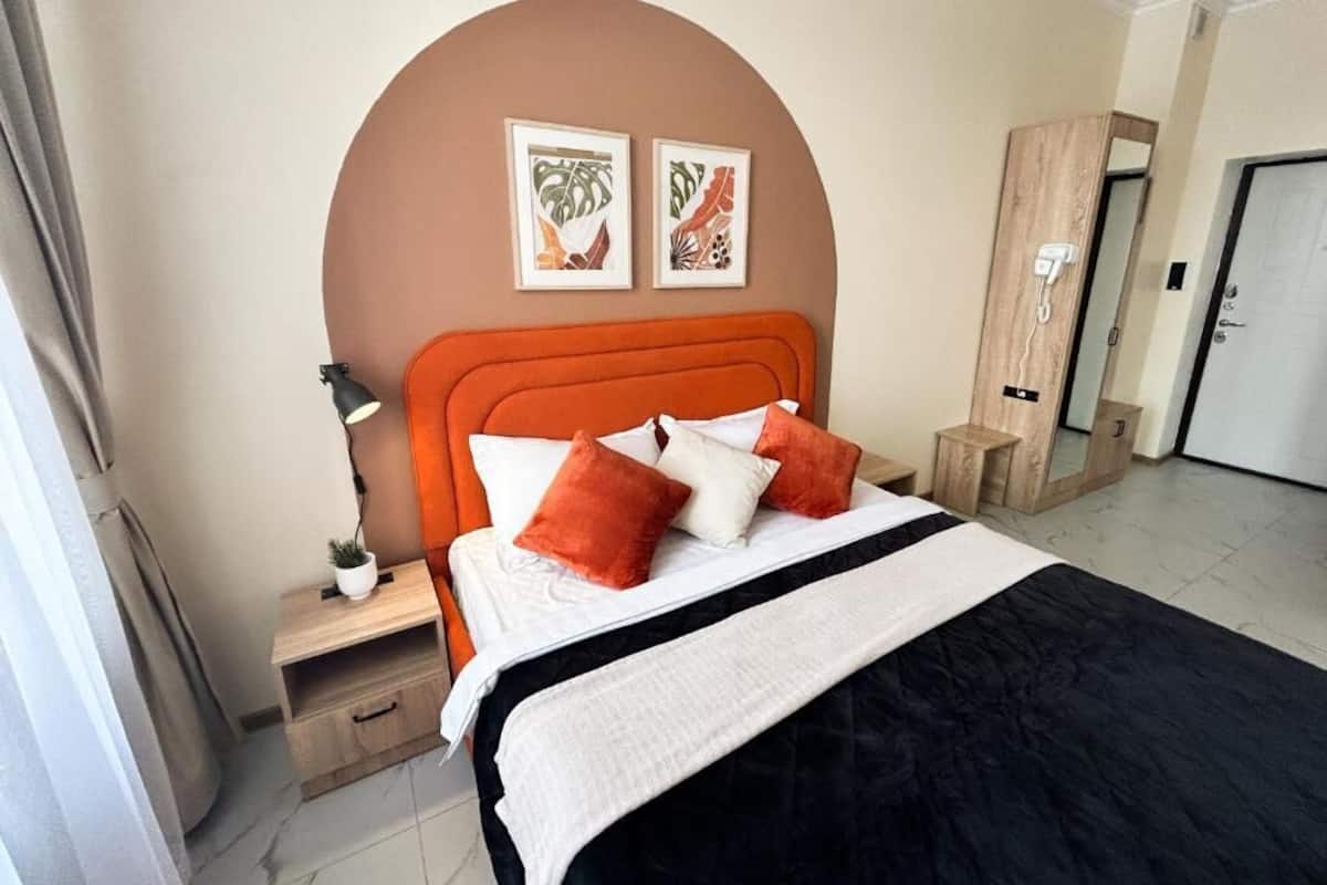 A hotel room with a bed, a nightstand, a lamp, a mirror, and two framed pictures on the wall.