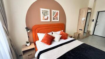 A hotel room with a bed, a nightstand, a lamp, a mirror, and two framed pictures on the wall.