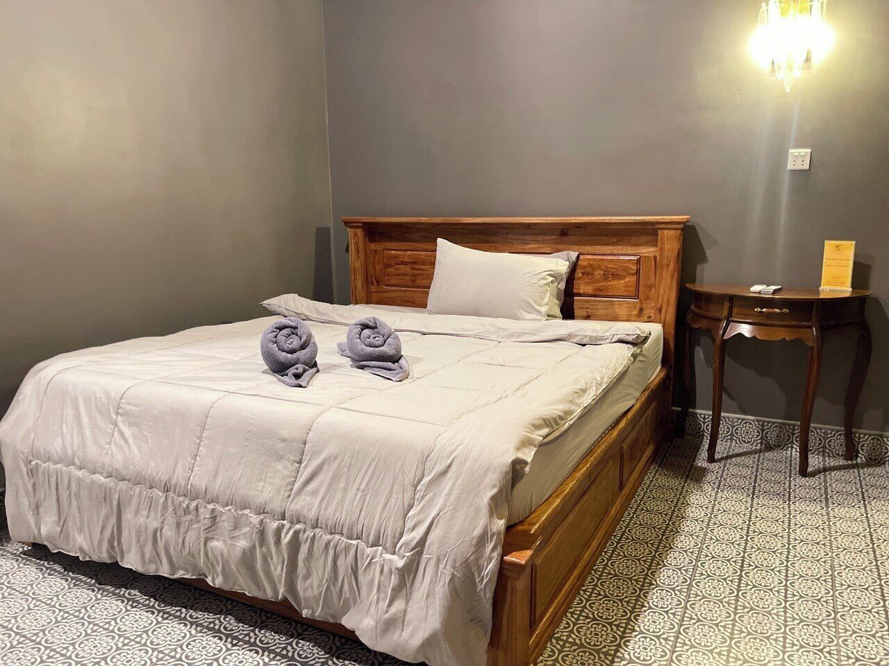 A single bed with a wooden headboard, a bedside table, and a wall-mounted light fixture.