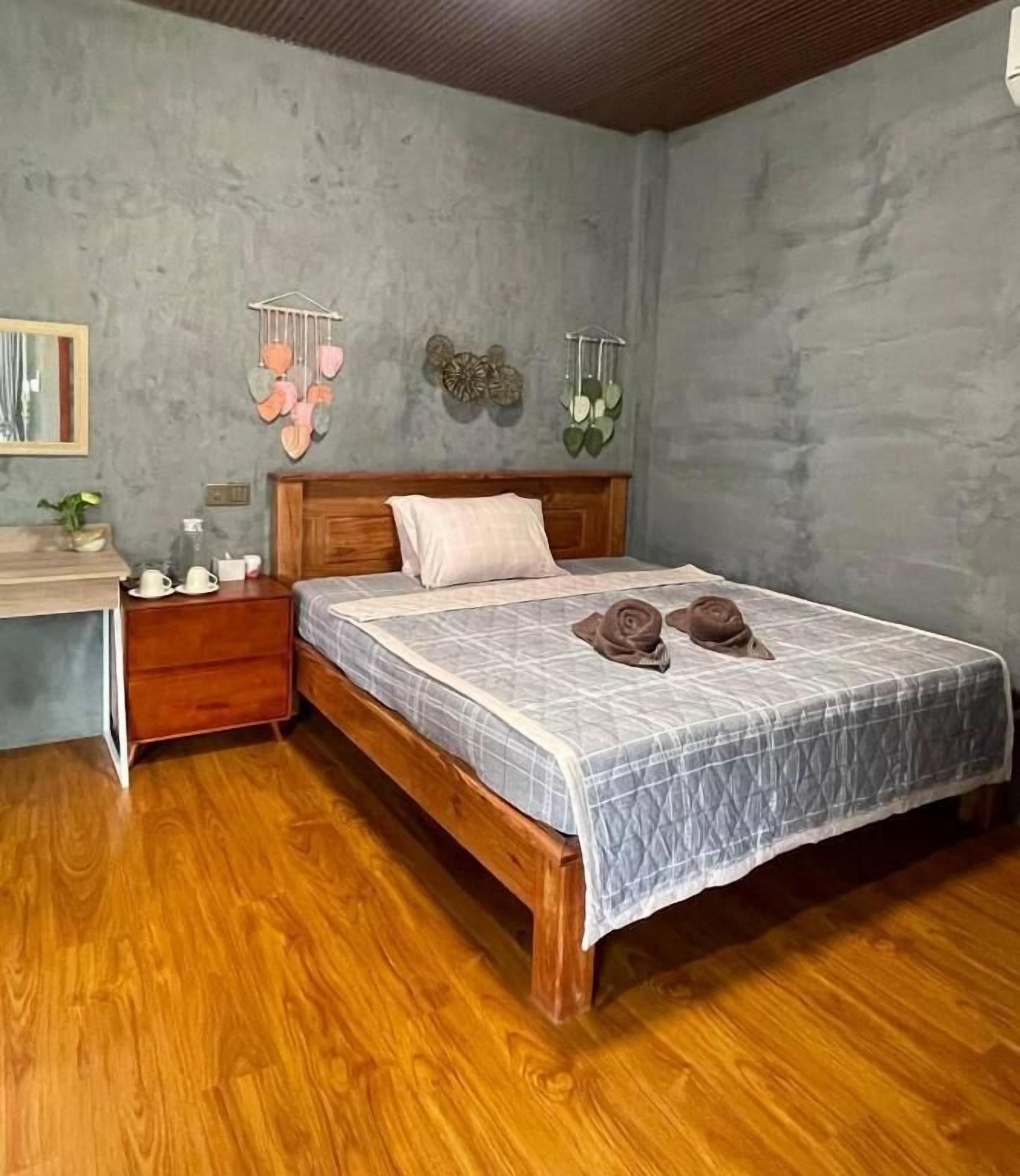 A bedroom with a wooden bed, a bedside table, a small desk, and a mirror.