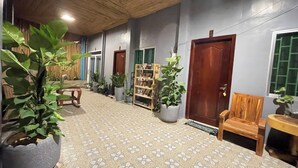 A hallway with potted plants, wooden furniture, and a patterned floor. - Mother's House (Battambang)