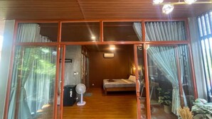 A room with a bed, a fan, and a view through large glass doors. - Mother's House (Battambang)