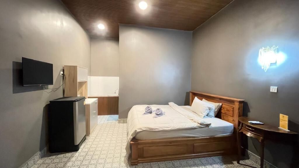 A bedroom with a bed, a television, a desk, and a wall-mounted light fixture.