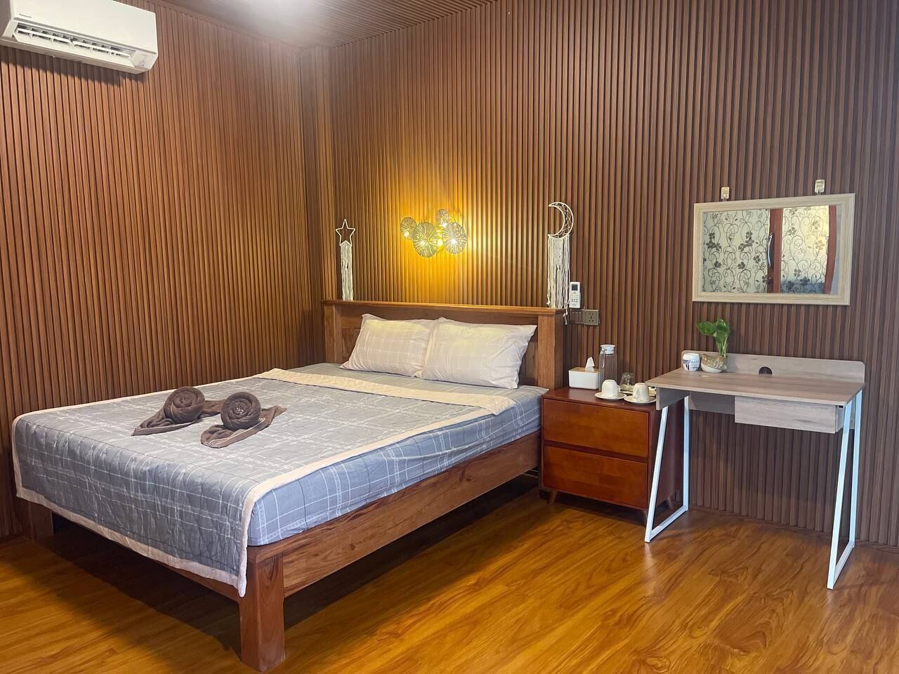 A wooden-paneled room with a bed, bedside table, desk, and wall-mounted air conditioning unit.