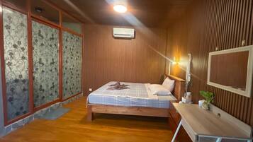 A bedroom with a wooden ceiling, a bed with a blue and white bedspread, a bedside table with a lamp, and a window with patterned curtains.