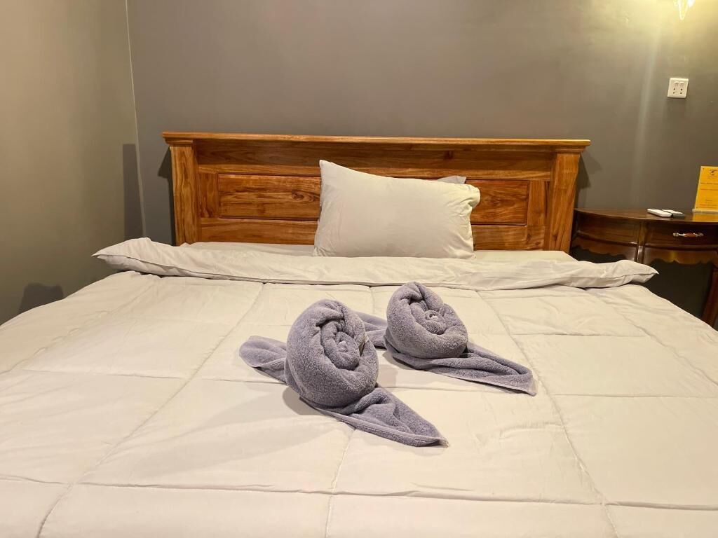 A bed with a wooden headboard, a white pillow, and two towels on the bed.