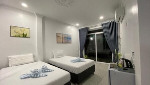 A hotel room with two beds, a small desk, and a sliding glass door leading to a balcony. - Mother's House (Battambang)
