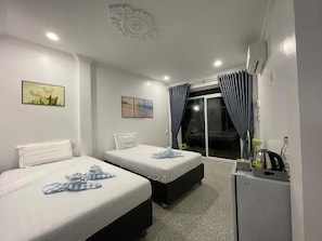 Una habitación de hotel con dos camas, un escritorio pequeño y un ventanal corredero que da a un balcón.