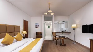 Habitación de hotel con cama, mesita de noche, lámpara, silla, escritorio y televisor.