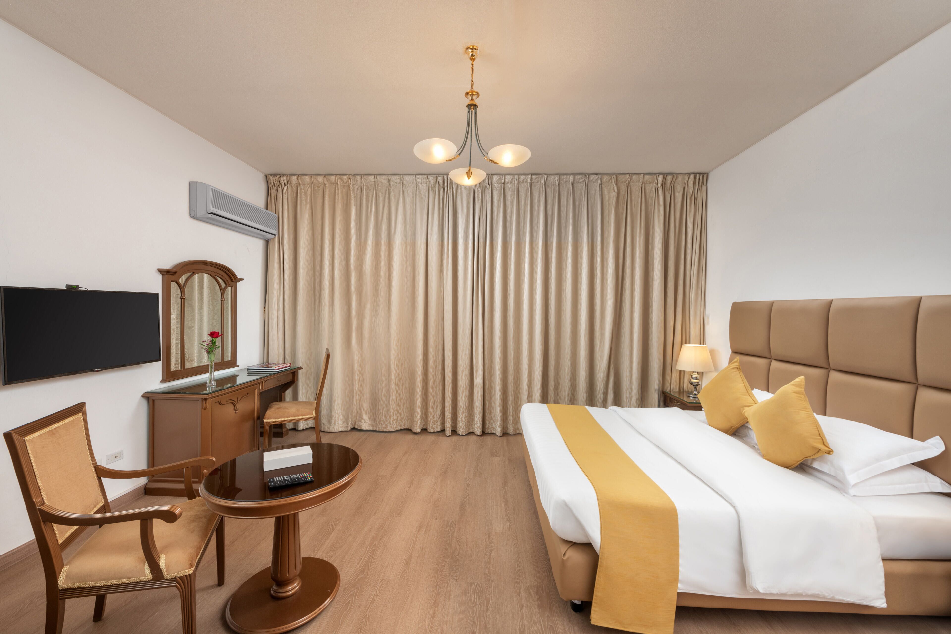 A hotel room with a bed, a desk, a chair, a television, and a window with curtains.