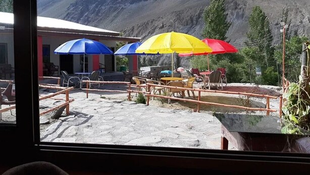 A view of a restaurant with outdoor seating, a bell hanging above, and a mountainous backdrop.