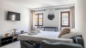 Ein modernes Hotelzimmer mit Bett, Fernseher, Schreibtisch und einem Fenster mit Vorhängen.