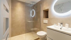 Ein modernes Badezimmer mit einer Duschkabine, Toilette, Waschbecken mit Pflegeprodukten und einem wandmontierten Spiegel.