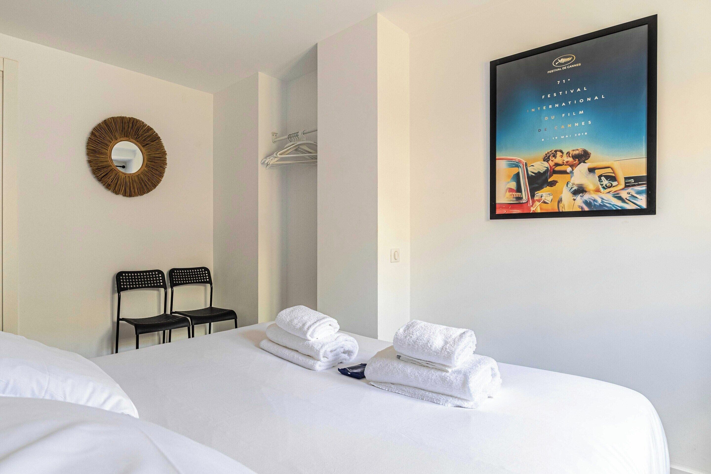 Una habitación de hotel con una cama, dos sillas, un espejo en la pared y un cartel.