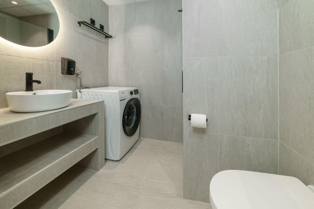 A modern bathroom with a sink, mirror, washing machine, and toilet.