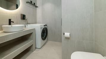 A modern bathroom with a sink, mirror, washing machine, and toilet.
