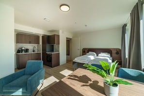 Ett hotellrum med en säng, ett skrivbord, en stol, ett litet pentry och en krukväxt.