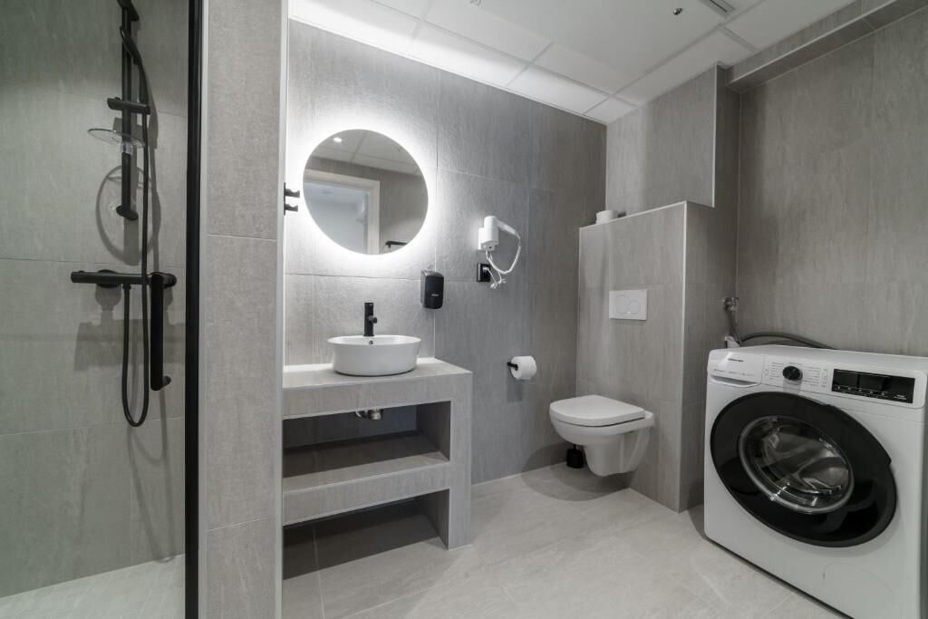 Een moderne badkamer met een ingebouwde wasmachine, een ronde spiegel en een toilet.