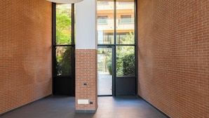 Un pasillo con paredes de ladrillo, ventanas grandes y una puerta que da al exterior.