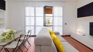 Una sala de estar moderna con un sofá, una mesa de comedor con sillas, un televisor y un ventanal grande.
