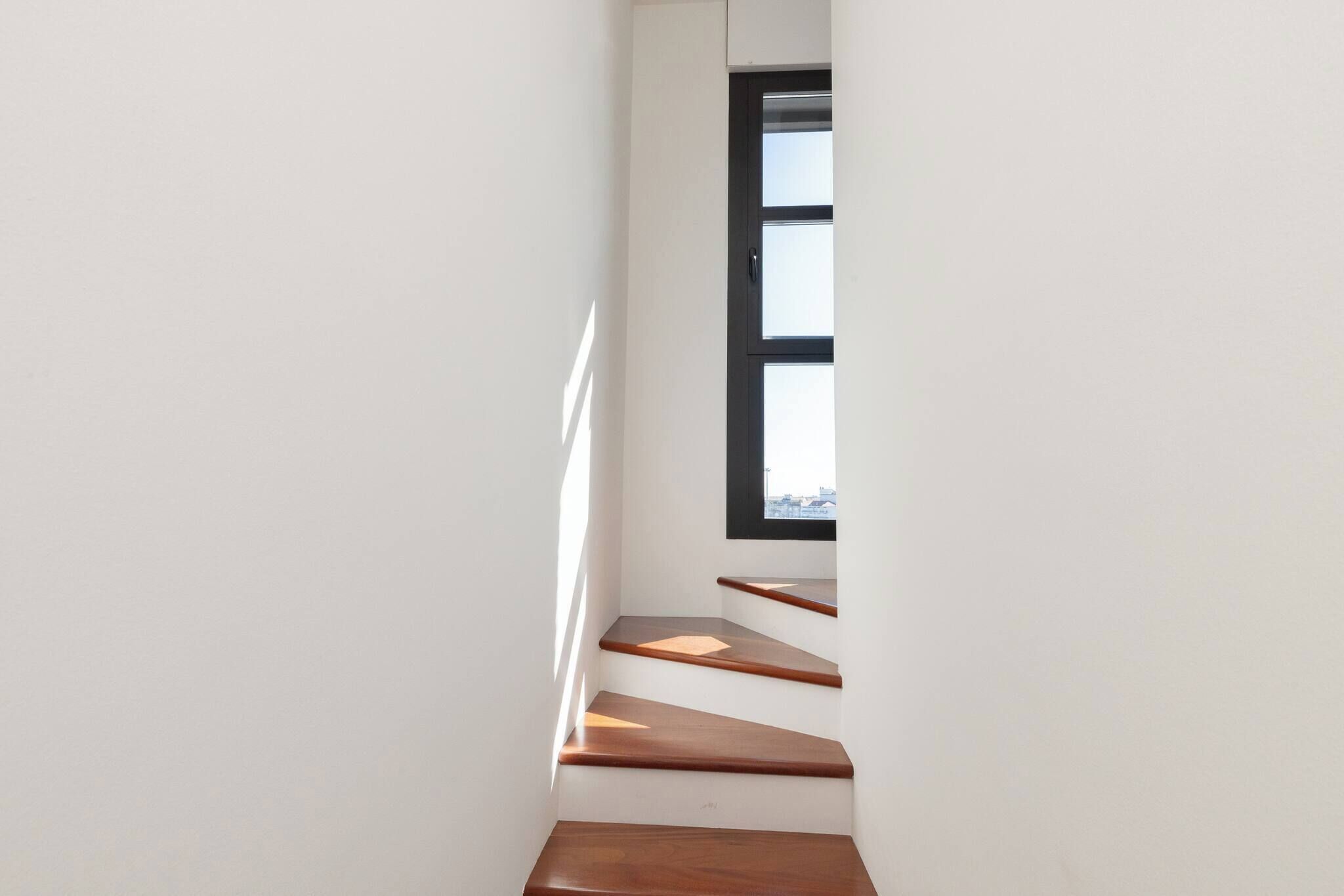 Un escalier étroit avec des marches en bois menant à une fenêtre.