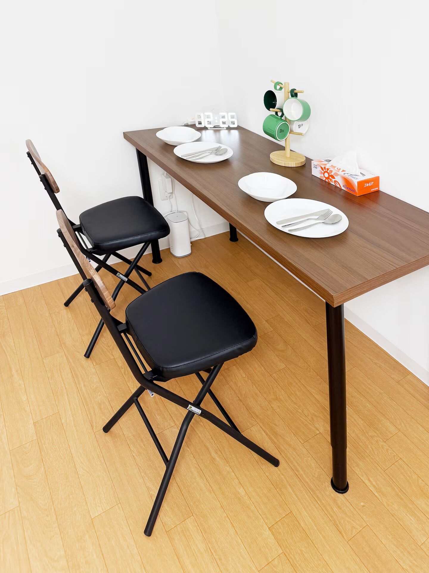 A dining table with four plates, two black chairs, a clock, and a tissue box.